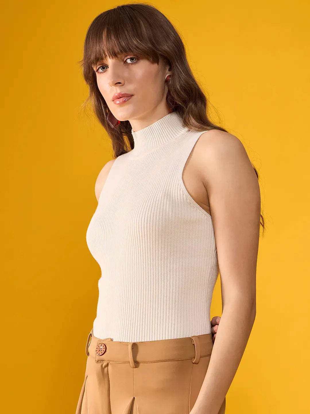 Woman with long brown hair in a 98degreenorth Off-White Ribbed High Neck Sleeveless Knit Top and tan pants.