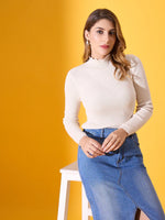 Woman wears 98degreenorth’s off white ribbed turtleneck sweater with denim skirt, standing by a stool on yellow background.