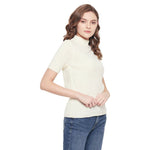 Woman with wavy brown hair in a 98degreenorth off white slim fit ribbed turtle neck sweater and blue jeans, standing sideways.