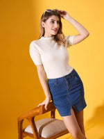 Woman wears 98degreenorth off white stretchable ribbed turtle neck sweater and denim skirt, smiling by a wooden chair.
