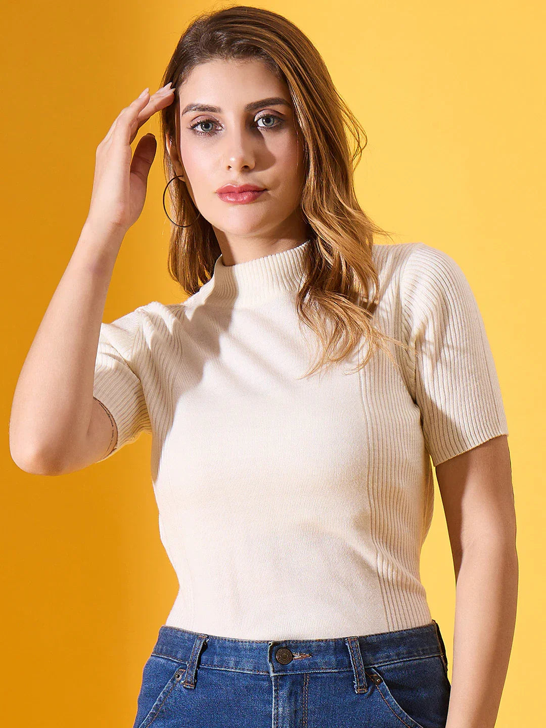 Woman wears 98degreenorth Off White Slim Fit Ribbed Turtle Neck Sweater with blue jeans, touching her hair.