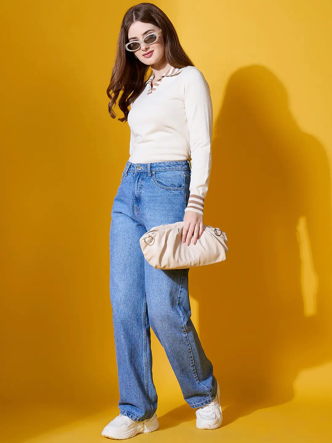 Woman in sunglasses, jeans, and sneakers wears a 98degreenorth off-white striped collar knit sweater, holding a beige clutch.