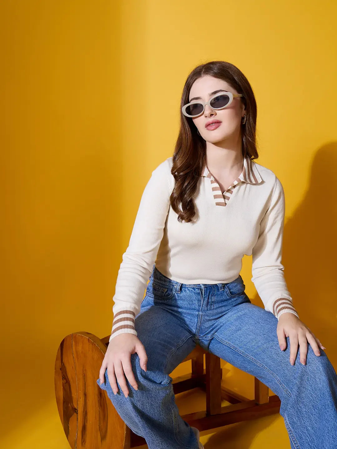 Woman in quiet luxury: 98degreenorth Off-White Striped Collar Knit Sweater, blue jeans, sunglasses; yellow backdrop.