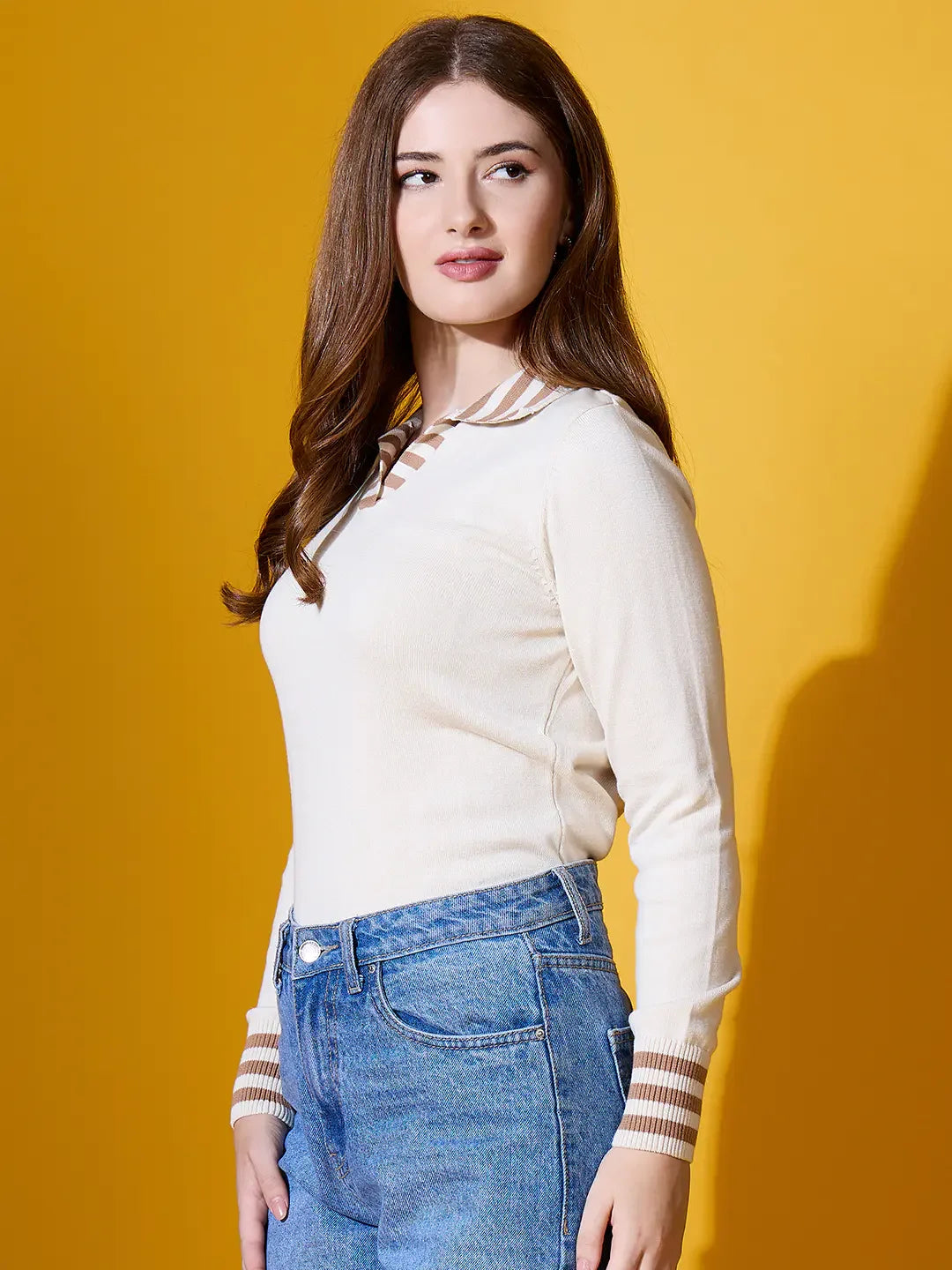 A woman in a 98degreenorth off-white striped collar knit sweater and blue jeans stands against a yellow background.
