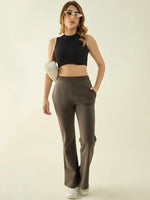 Woman in black crop top, 98degreenorth olive flared bootcut trousers, white sneakers, and sunglasses poses stylishly.