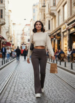 A woman in 98degreenorth Olive Flared Bootcut Cotton Stretchable Trousers strolls a city street with a shopping bag.