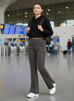 A woman in a black hoodie and 98degreenorth Olive Green Bootcut Sweatpants stands at the airport with a backpack.