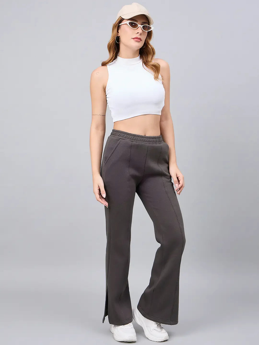 Woman in a white crop top, 98degreenorth olive green flared lounge pants, white sneakers, beige cap, and glasses.
