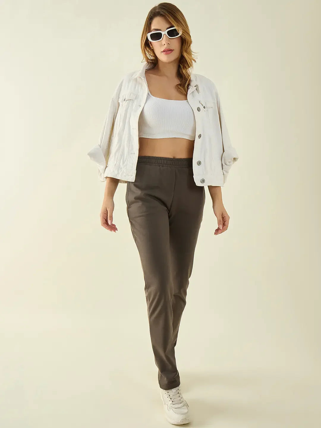 Woman in white crop top, jacket, 98degreenorth Olive Cotton Stretchable Trousers, white sneakers, and sunglasses posing confidently.