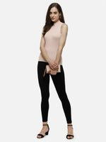 Woman in a pink ribbed high neck sleeveless knit top by 98degreenorth, black leggings, heels, and a beige clutch.