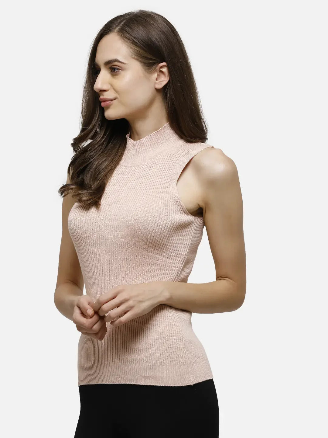 Woman in a 98degreenorth pink ribbed high neck sleeveless knit top with black pants, standing and looking aside.