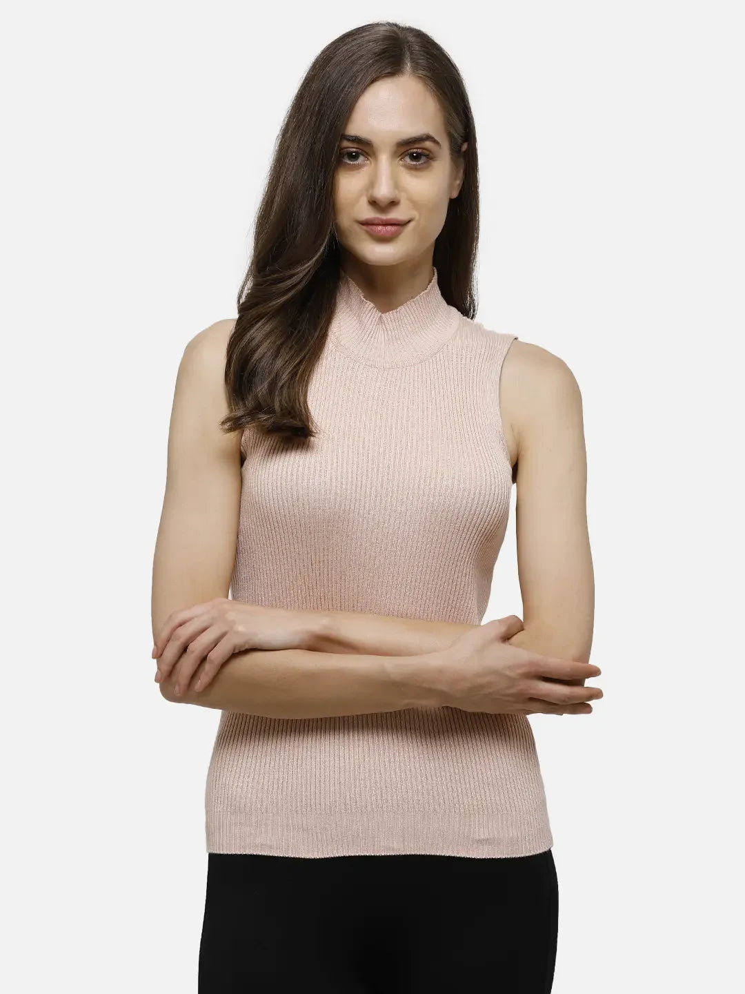 Woman with long brown hair in 98degreenorth's pink ribbed high neck sleeveless knit top and black pants, arms crossed.