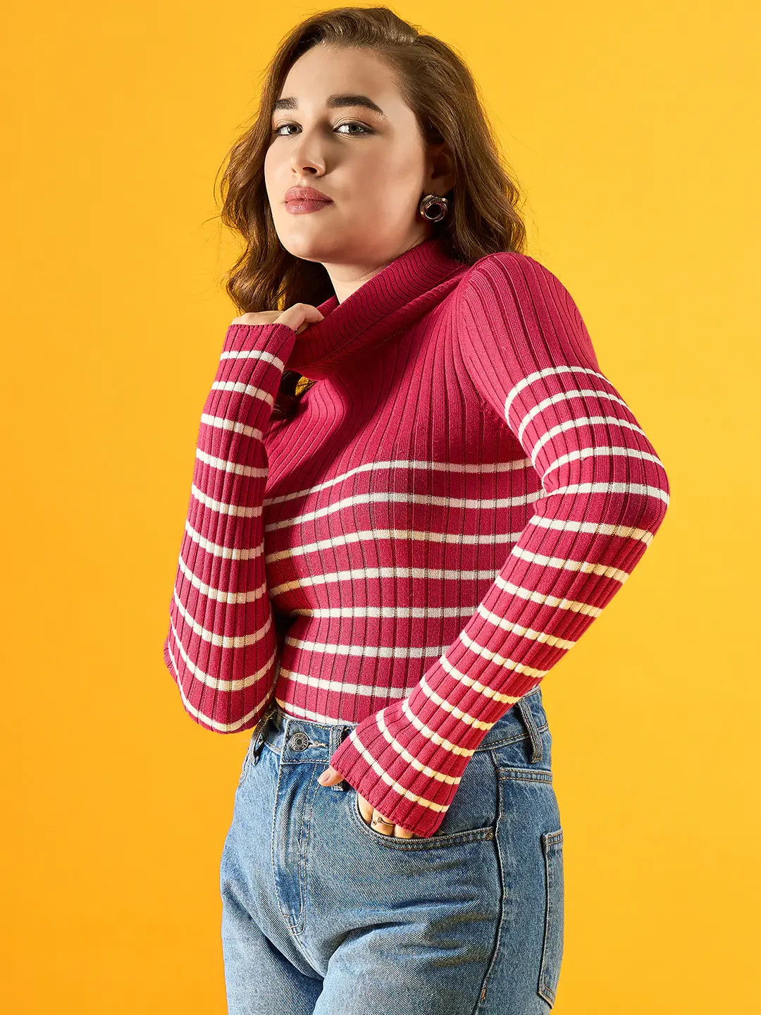 A woman wears a 98degreenorth Women’s Pink Ribbed Striped Turtleneck Sweater, posing against a yellow background.