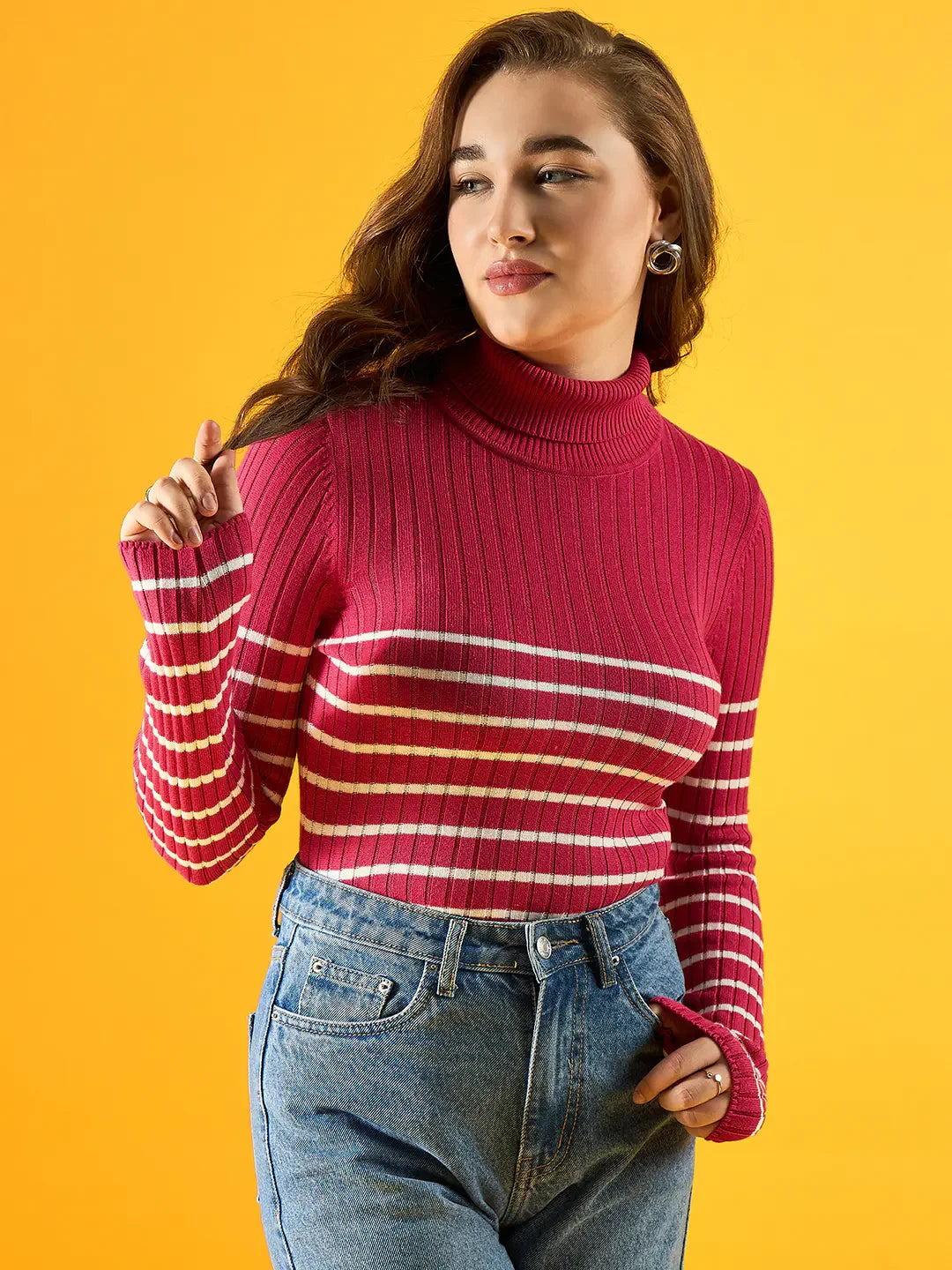 Woman in a 98degreenorth pink ribbed striped turtleneck sweater stands against yellow, looking to the side.
