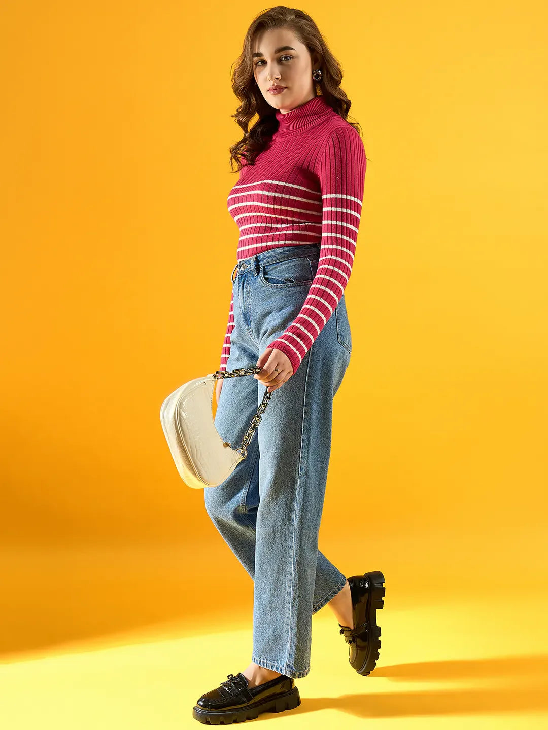 Woman in a 98degreenorth pink ribbed striped turtleneck sweater, blue jeans, and black shoes holding a white handbag.