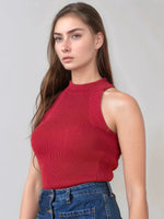 Woman with long brown hair wears a 98degreenorth red ribbed halter neck sleeveless knit top and blue jeans, on gray background.
