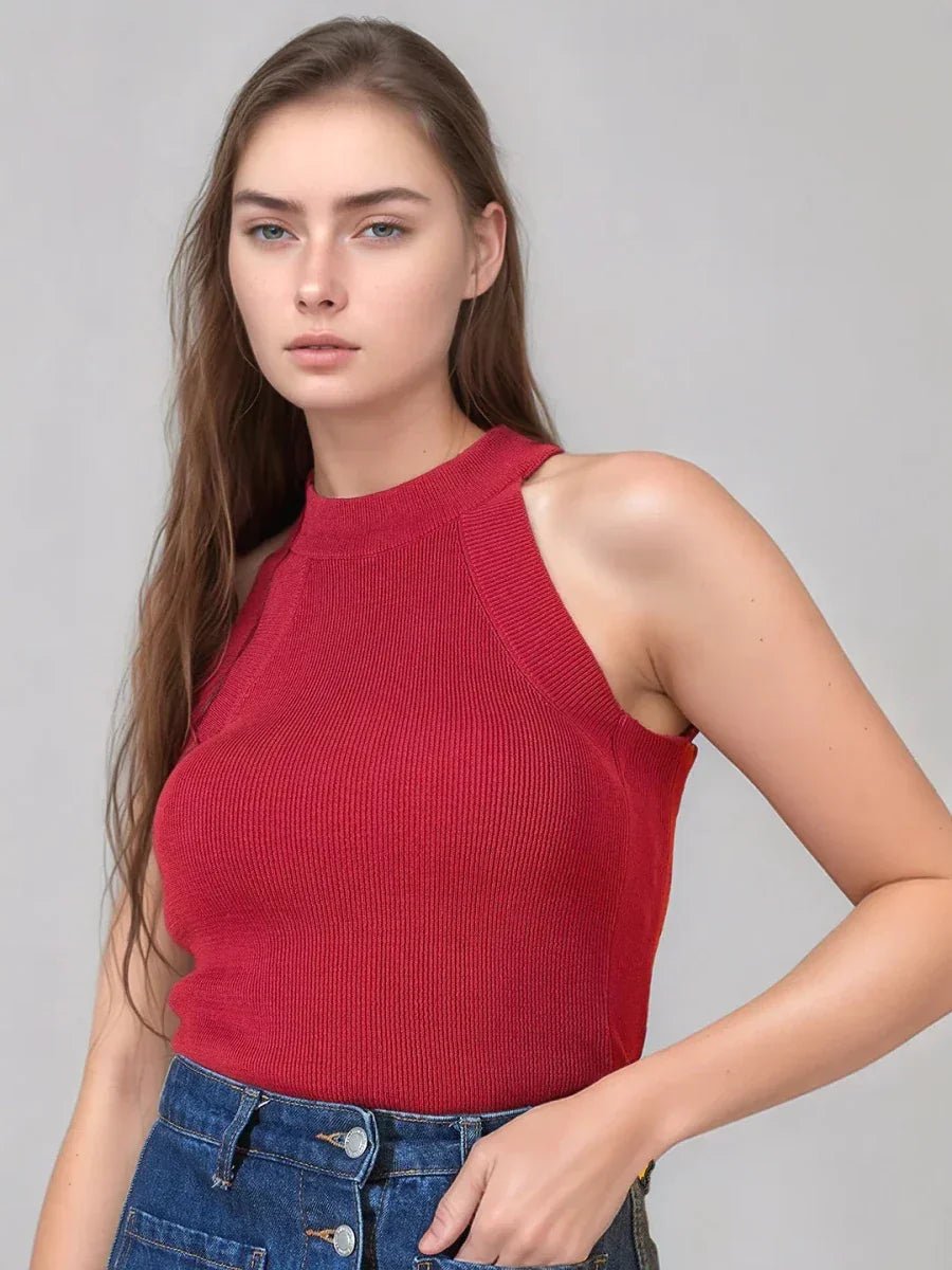 Woman in 98degreenorth’s Red Ribbed Halter Neck Sleeveless Knit Top, paired with blue denim pants, stands against a plain background.