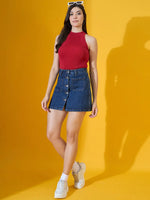 A woman wears the 98degreenorth Women’s Red Ribbed Halter Neck Knit Top, styled for a party, against a yellow background.