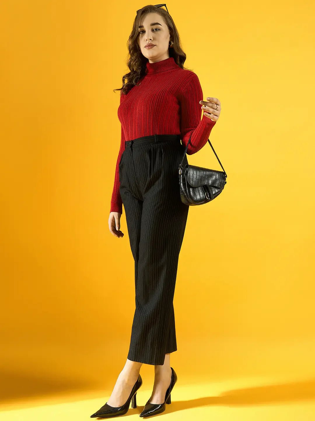 Woman in 98degreenorth’s red ribbed turtleneck sweater poses with a black bag against a yellow background.