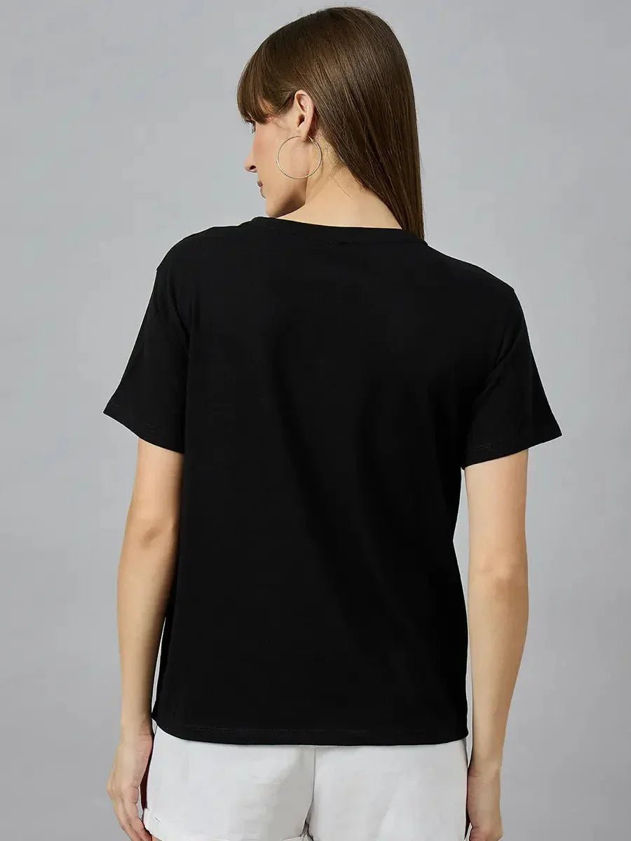 Woman with long brown hair in a 98degreenorth Typography Print Cotton T-shirt and white shorts, seen from the back.