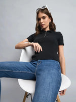 Woman in a 98degreenorth black ribbed half-zip polo crop top and jeans sits on a white chair, leaning back.