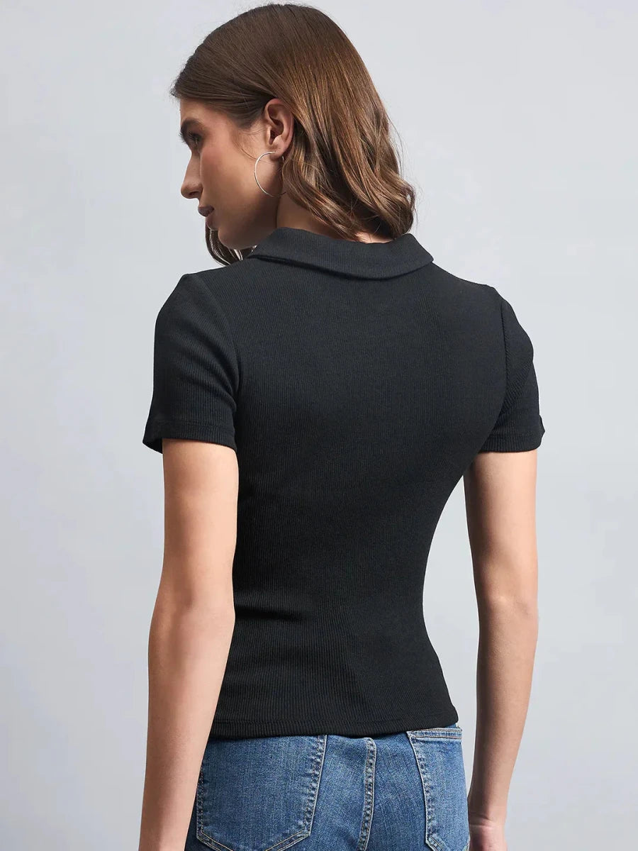 Woman with brown hair in a 98degreenorth black ribbed half-zip polo crop top and blue jeans, back to camera.