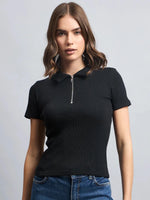 Woman with wavy brown hair in a 98degreenorth black ribbed half-zip polo crop top and blue jeans, against a gray background.