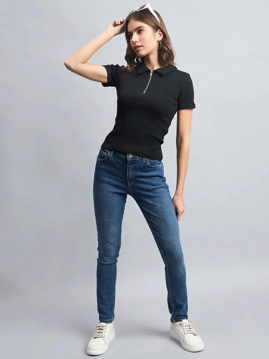 Woman wears 98degreenorth Ribbed Half-Zip Polo Top in black, blue jeans, and white sneakers against a gray background.