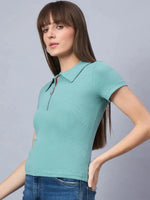 Woman in a 98degreenorth sea green ribbed half-zip polo crop top and blue jeans, against a gray background.