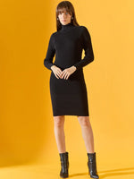 A woman in a 98degreenorth Women’s Ribbed Knitted Bodycon Dress – Black pairs it with ankle boots on a yellow backdrop.