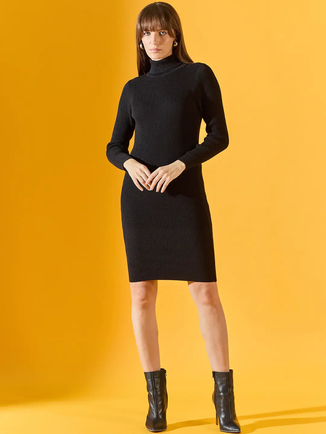 A woman in a 98degreenorth Women’s Ribbed Knitted Bodycon Dress – Black pairs it with ankle boots on a yellow backdrop.