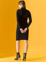 Woman in a 98degreenorth black ribbed bodycon turtleneck dress stands on yellow, facing away.