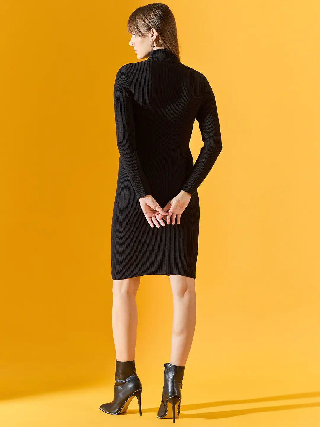 Woman in a 98degreenorth black ribbed bodycon turtleneck dress stands on yellow, facing away.