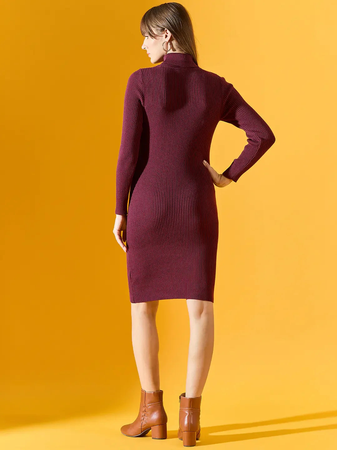 A woman in a 98degreenorth ribbed burgundy turtleneck sweater dress and brown boots stands against a yellow background.