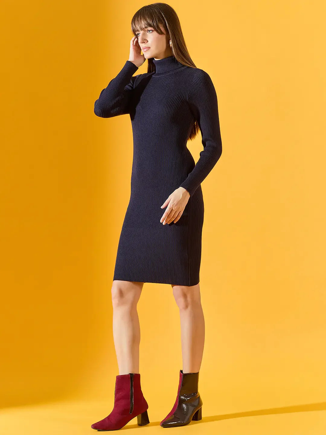 A woman wears a 98degreenorth navy ribbed bodycon turtleneck dress, standing against a yellow background.