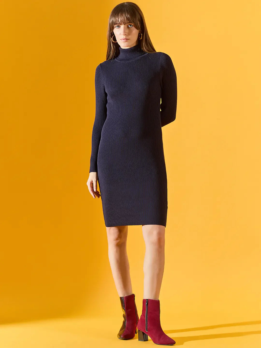 Model wears 98degreenorth Women’s Ribbed Knitted Bodycon Dress – Navy, styled with red ankle boots on a yellow backdrop.
