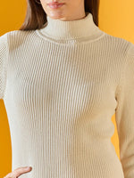 A woman wears the 98degreenorth off-white ribbed knitted bodycon turtleneck dress against an orange background.