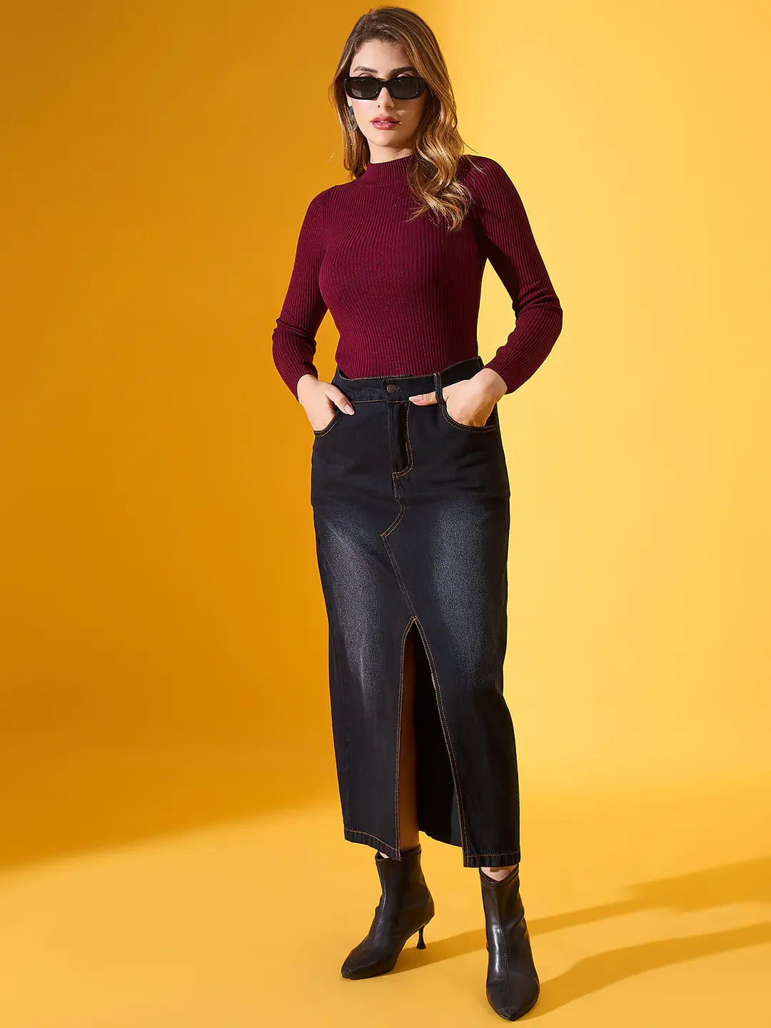 Woman in a 98degreenorth rosewood ribbed high-neck sweater and black skirt, boots, sunglasses on a yellow background.
