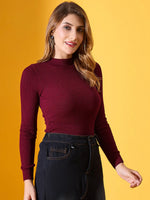 Woman wears 98degreenorth Rosewood Ribbed High-Neck Sweater with high-waisted pants before a yellow backdrop.