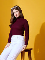Woman wears 98degreenorth’s Rosewood Ribbed Turtle-Neck Pullover, seated on a stool against a yellow background.