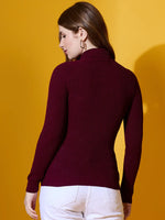 Woman wears 98degreenorth’s rosewood ribbed turtle-neck pullover and white pants, standing against a yellow background.