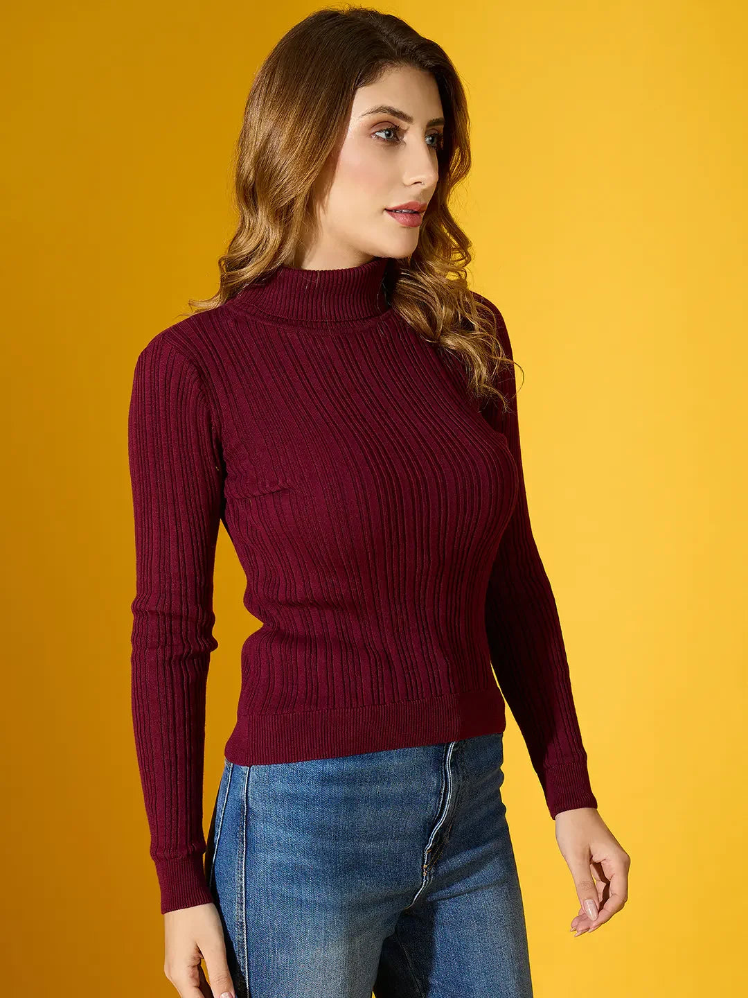 Woman in 98degreenorth’s rosewood ribbed turtleneck sweater and blue jeans stands against a yellow background.