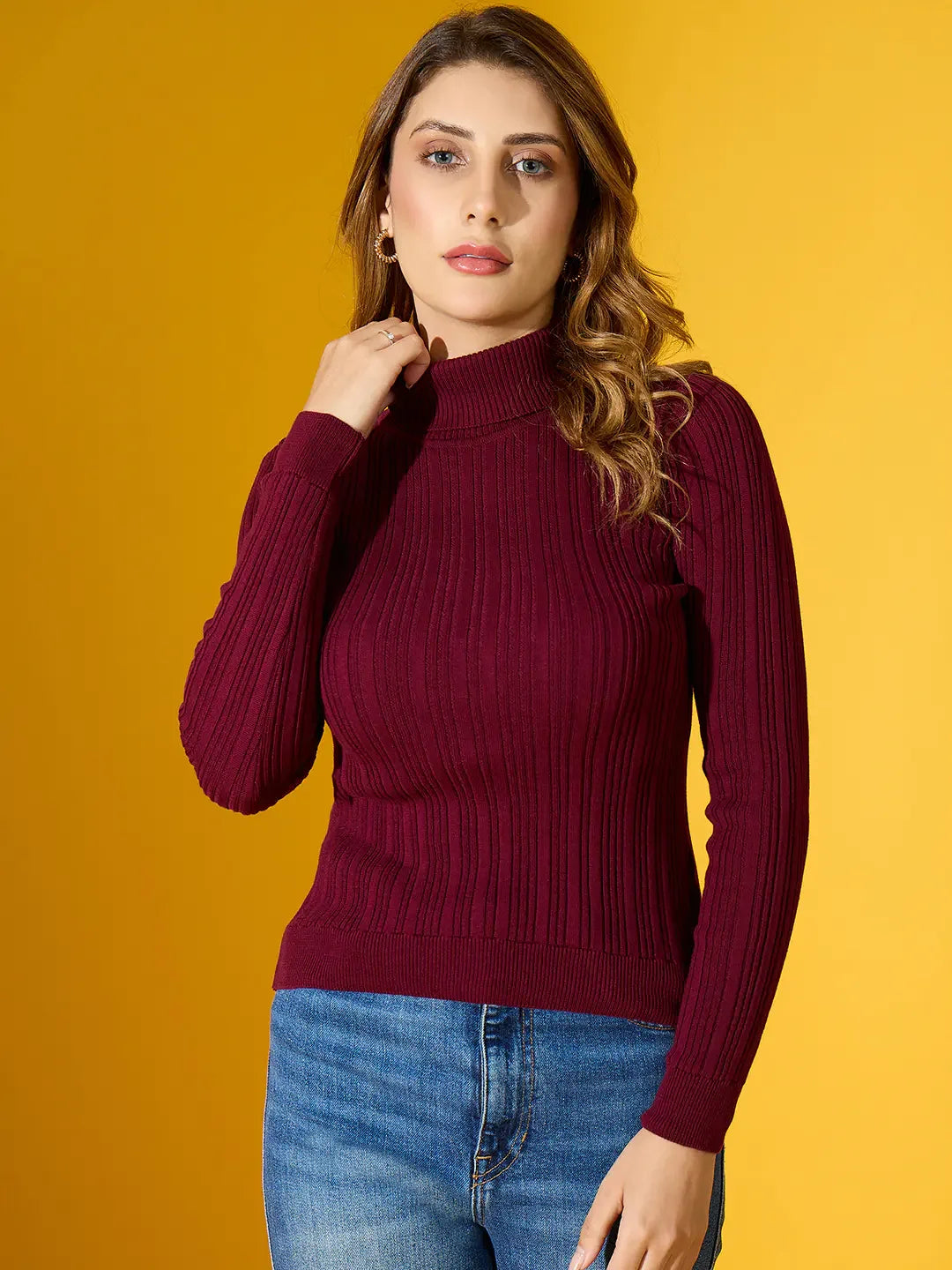Woman in a 98degreenorth Rosewood Ribbed Turtleneck Sweater and blue jeans stands against a yellow background.