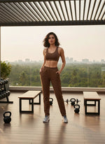 Woman in 98degreenorth’s rust cotton slim fit trackpants stands on a rooftop gym with a city view.