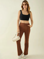 Woman in sunglasses wears a black crop top, 98degreenorth rust flared bootcut trousers, white sneakers, and a white handbag.