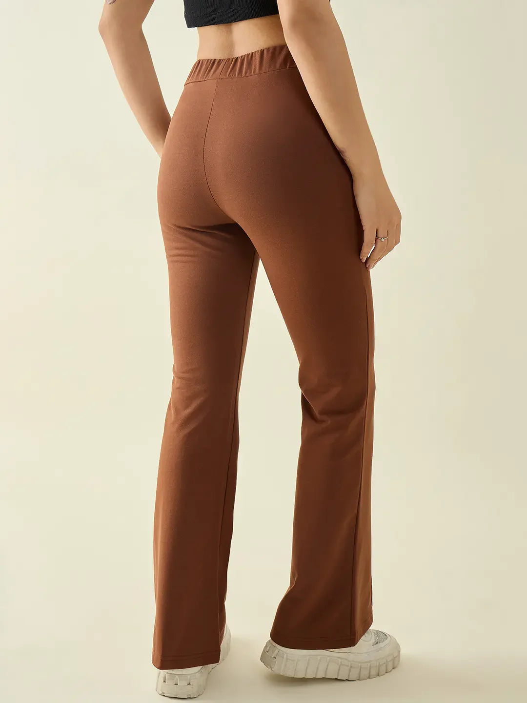 Model wears 98degreenorth Women’s Rust Flared Bootcut Cotton Stretchable Trousers, black crop top, and white sneakers.