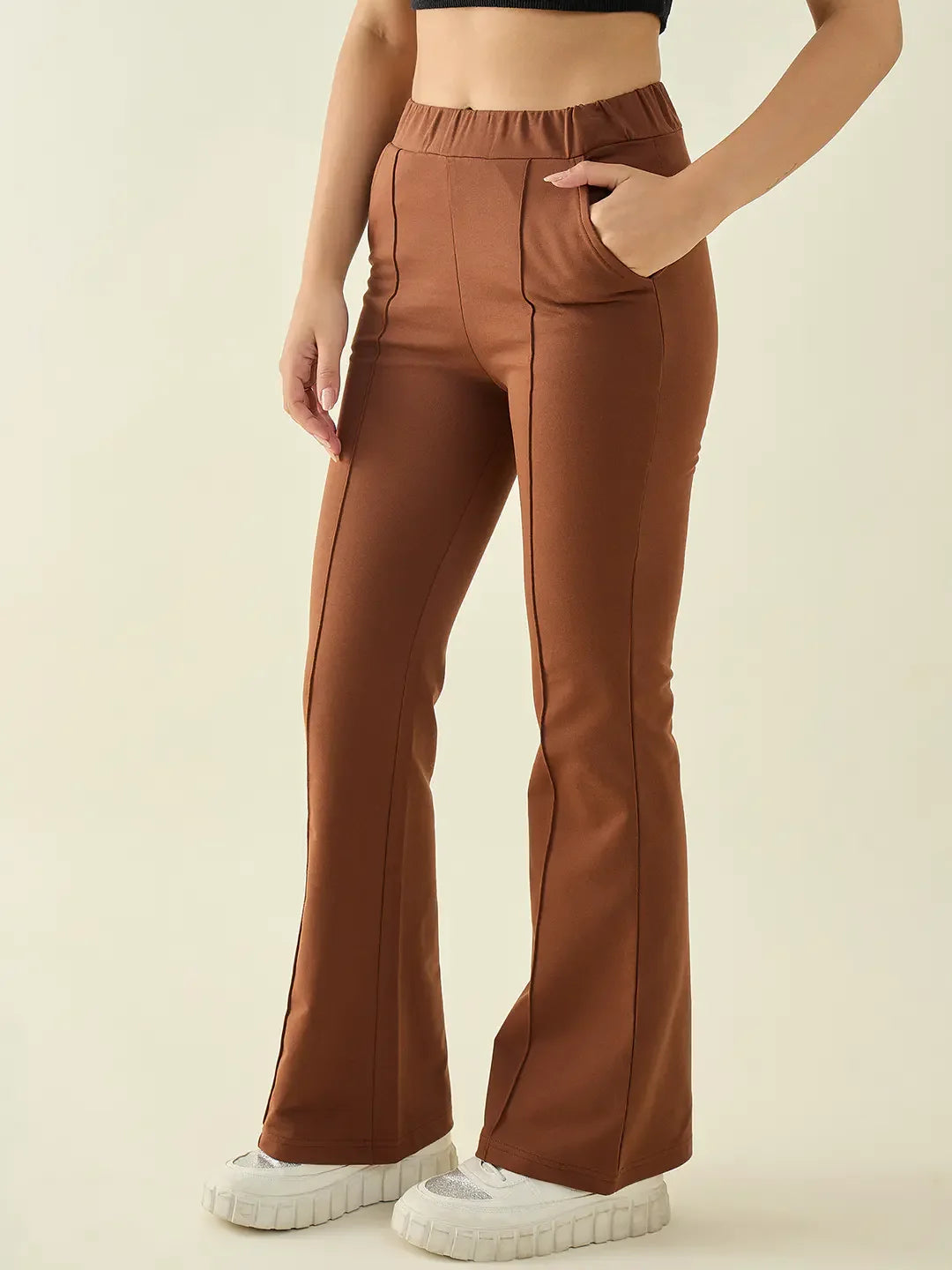 Wearing 98degreenorth Women’s Rust Flared Bootcut Trousers, white shoes, and a black crop top on a plain background.