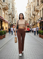 A woman in a beige crop top and 98degreenorth rust flared bootcut cotton stretchable trousers walks in the city.