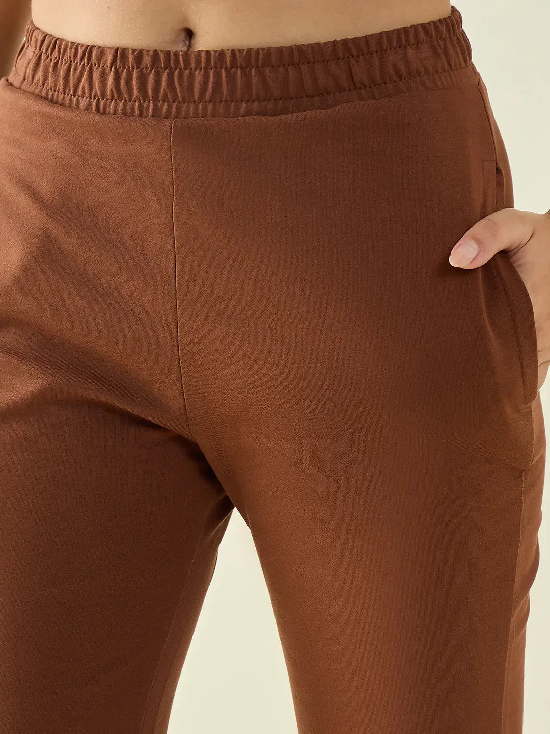 A person wears 98degreenorth Women’s Rust Flared Bootcut Stretchable Trousers with an elastic waistband, hand in pocket.