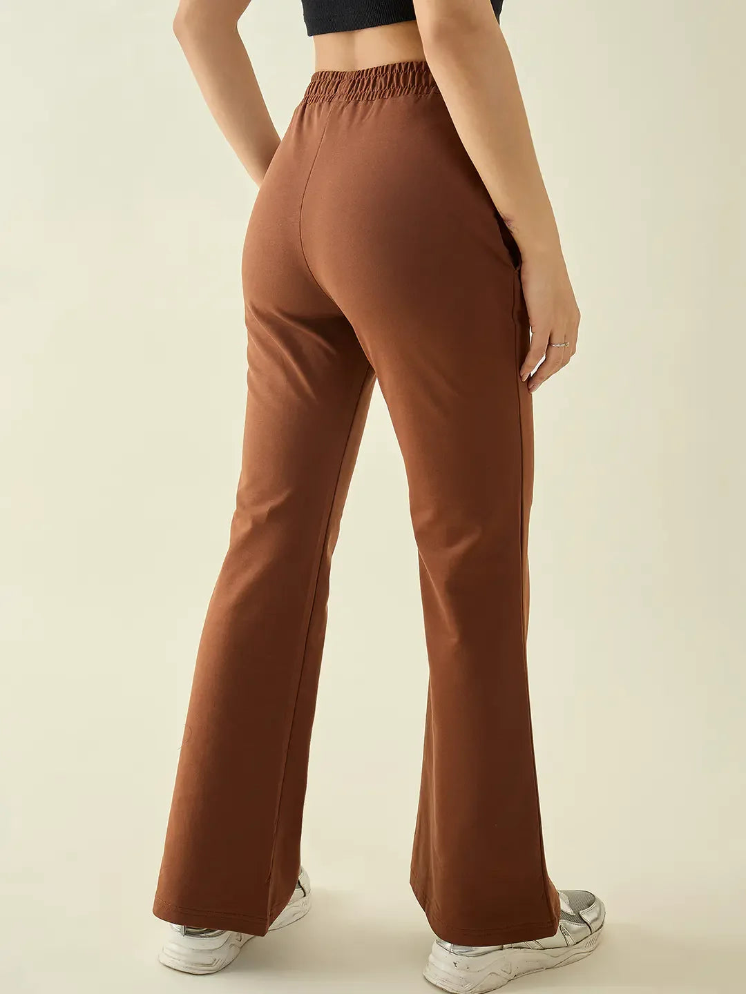Woman in 98degreenorth Rust Flared Fit Bootcut Cotton Stretchable Trousers, white sneakers, black crop top.